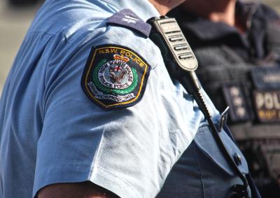 Close-up of a police officer walking along the street, showing their shoulder emblem